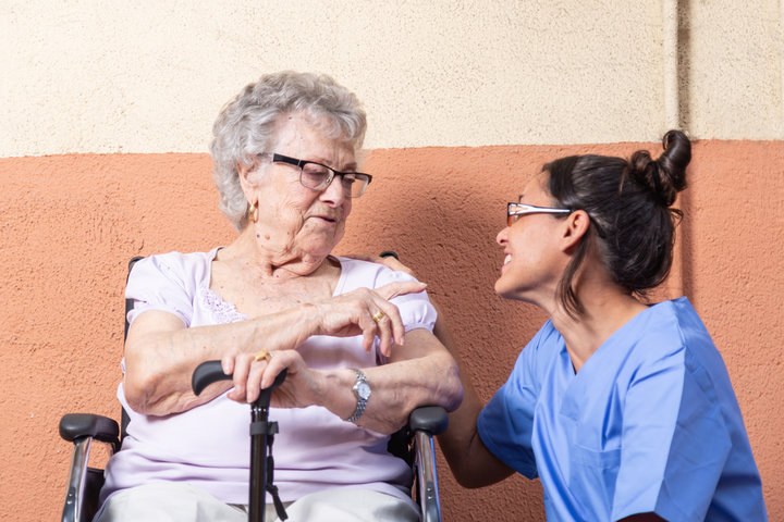 Happy Senior woman with walking stick in Wheelchair.with her caregiver at home .,They are talking and laughing together.
