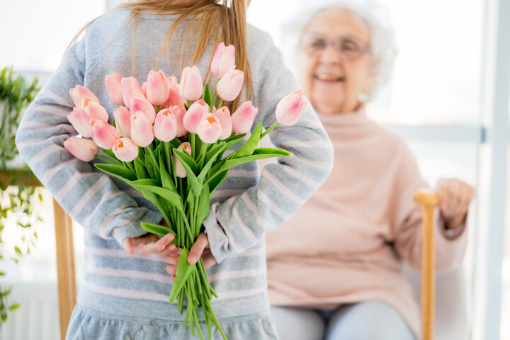 a grandchild visiting her grandma in a care home with flowers behind her back