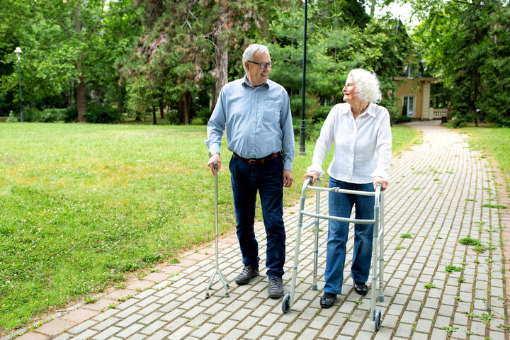 two seniors strolling with walking aids through a park