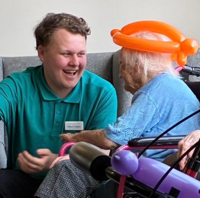 staff smiling with resident with a balloon on her head