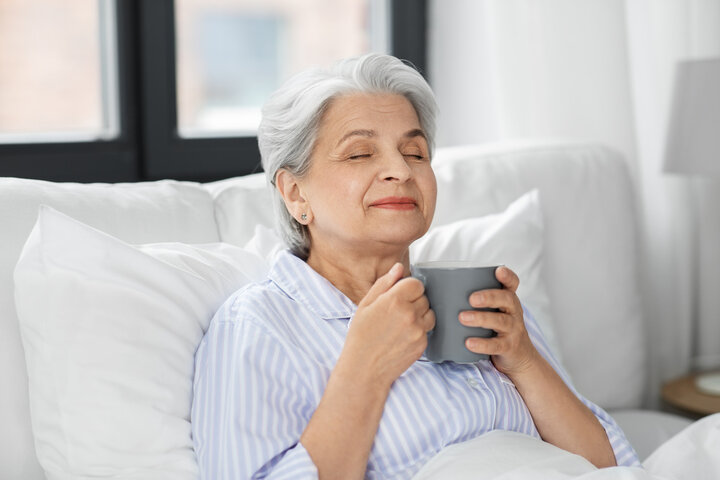 old woman smiling with coffee in bed at nursing home 