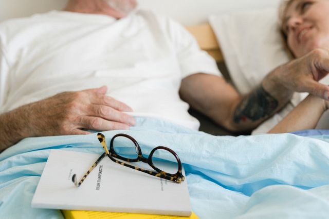 An elderly couple enjoying a peaceful moment in bed together, glasses resting on a book.